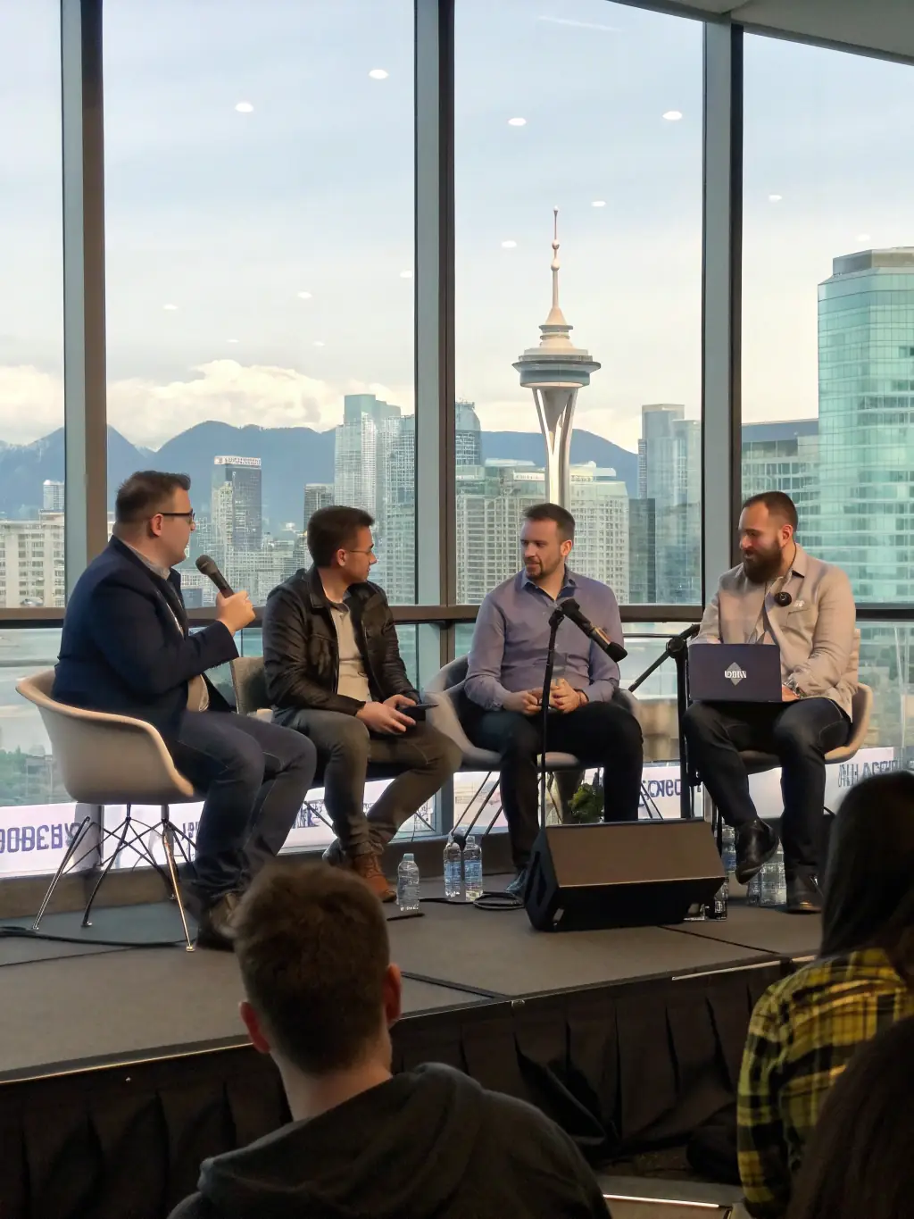 A dynamic shot of a panel discussion featuring leading Canadian tech entrepreneurs at the Annual Tech Innovation Conference in Vancouver, Canada, with the Vancouver skyline visible in the background.