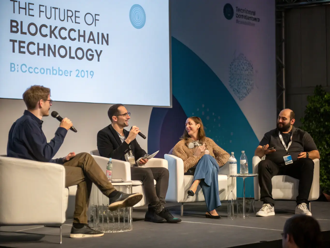 A dynamic image of a panel discussion in progress, featuring three speakers engaged in a lively debate on blockchain technology. The audience is attentive and diverse.